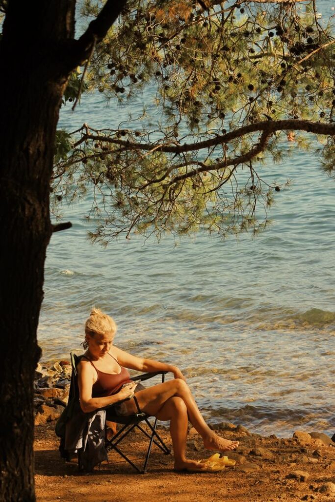 A woman enjoys a peaceful moment on a folding chair by the shore, soaking up the summer sun.
